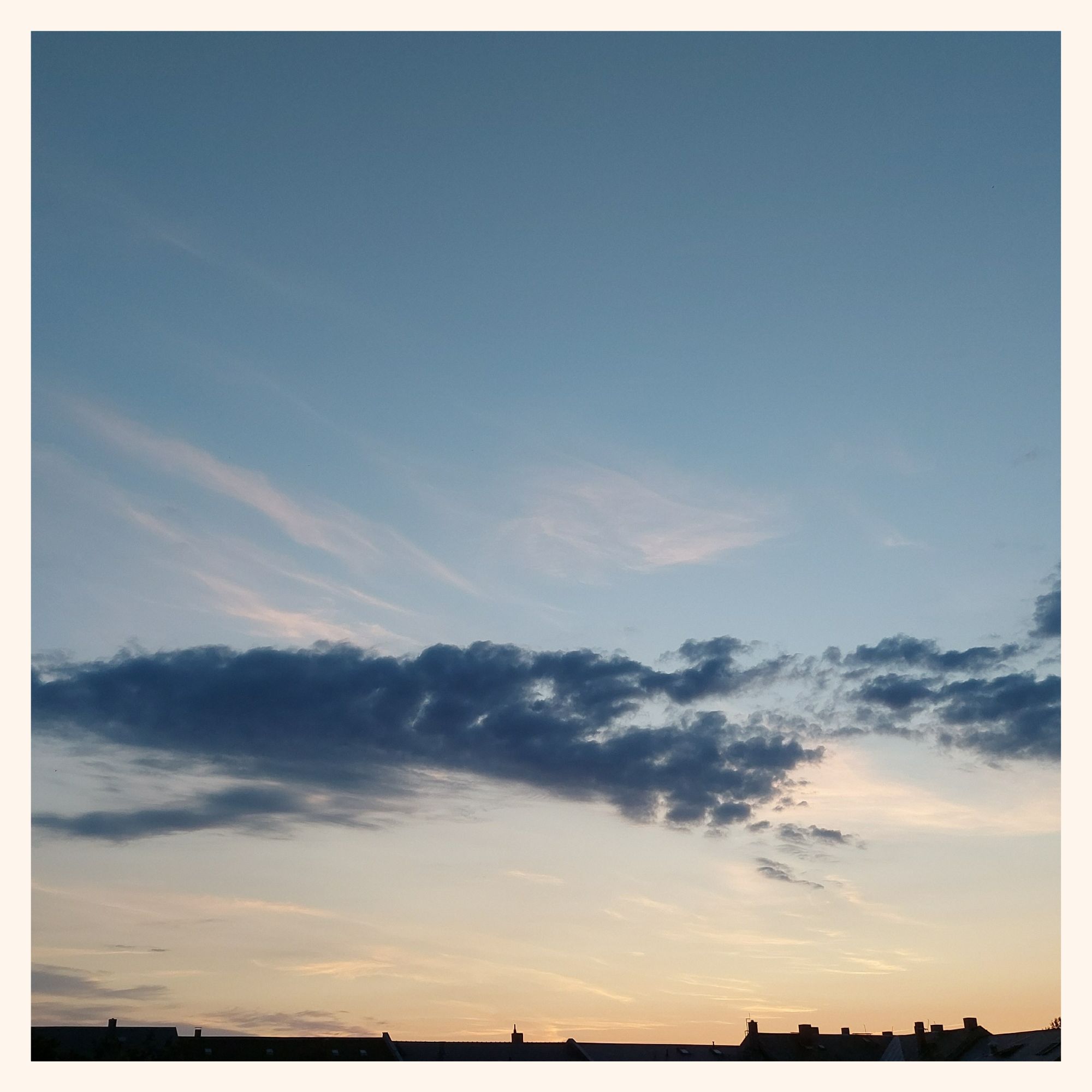 A very quiet morning sky, one line of clouds and the dark structure of city roofs.