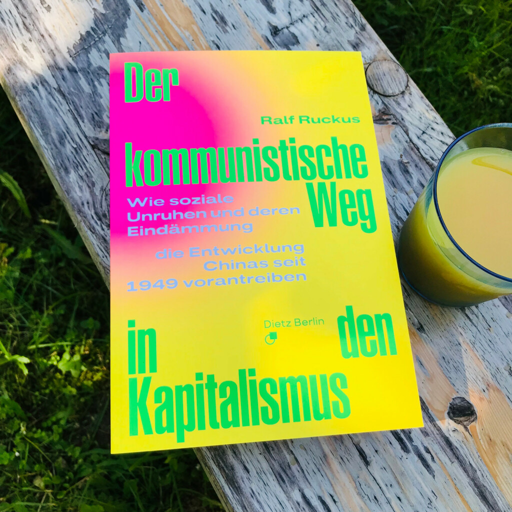 Bereit zur Lektüre auf die Gartenbank gelegt: »Der kommunistische Weg in den Kapitalismus. Wie soziale Unruhen und deren Eindämmung die Entwicklung Chinas seit 1949 vorantreiben« von Ralf Ruckus, daneben ein Kaltgetränk