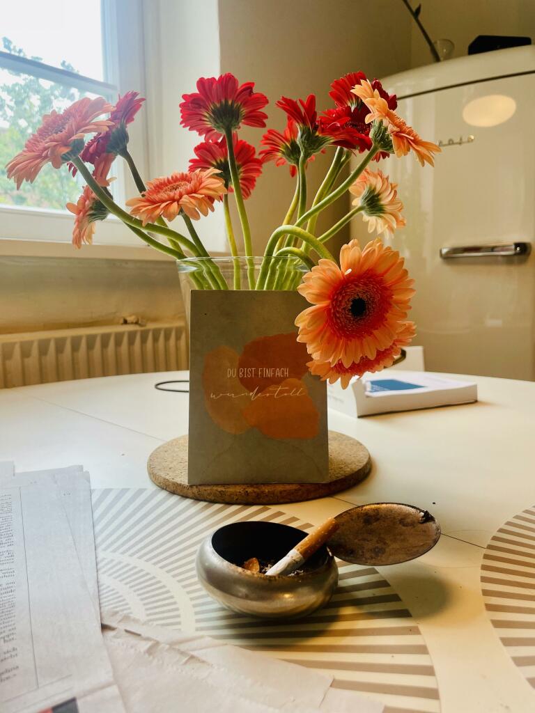 in Aschenbecher mit einer ausgedrückten Zigarette auf einem Tisch vor einer Vase mit Blumen.