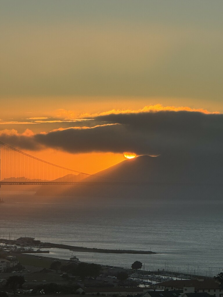 the sun sets behind low clouds over the pacific at golden gate bridge tonight