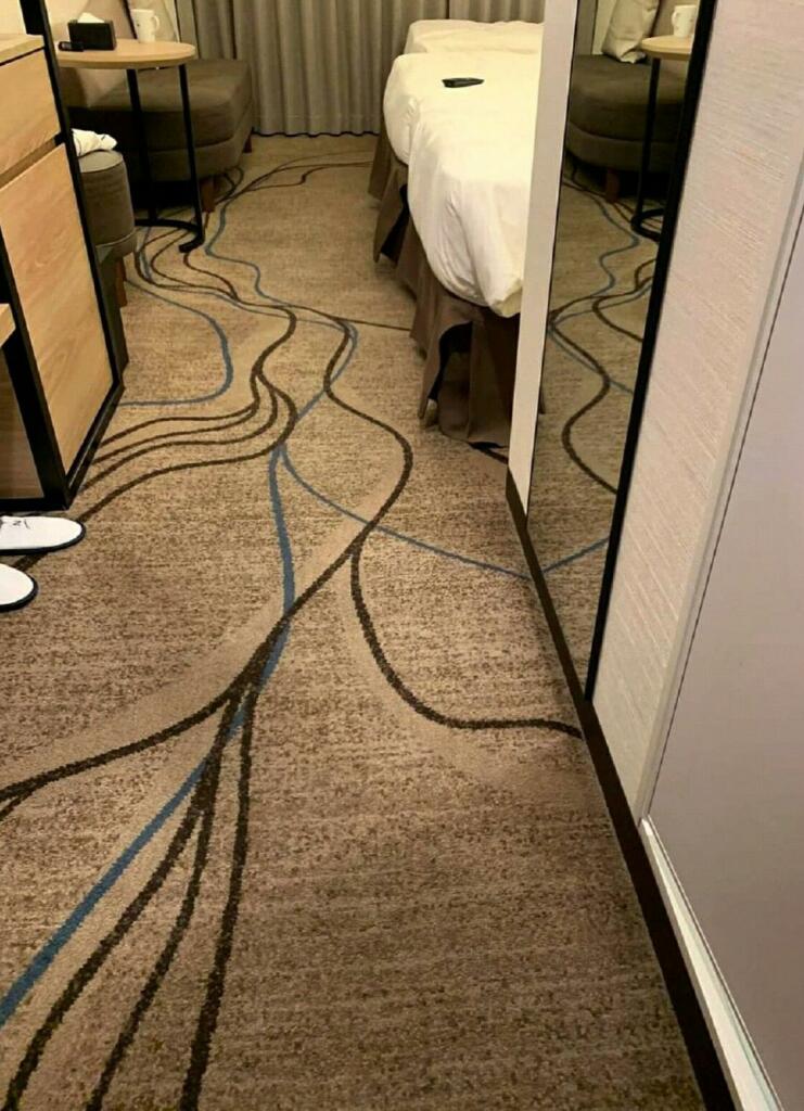 A hotel room with a brown carpet with 1 inch strands running in different colors, twisting and weaving and looking like disorganized cables on the floor