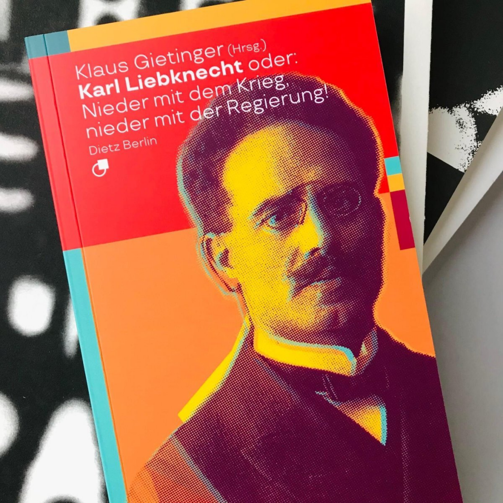 Cover unserer Biografischen Miniatur, auf einem Bücherstapel fotografiert: „Karl Liebknecht oder: Nieder mit dem Krieg, nieder mit der Regierung!“, herausgegeben von Klaus Gietinger