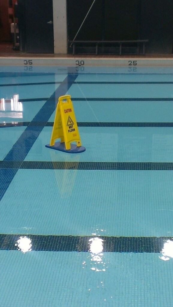 Caution Wet Floor sign on a paddle board floaty in the middle of the po