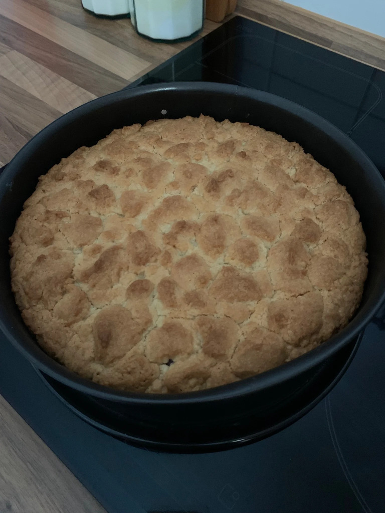 Ein runder Kuchen mit gebräunten Streuseln kühlt auf dem Kochfeld ab. 