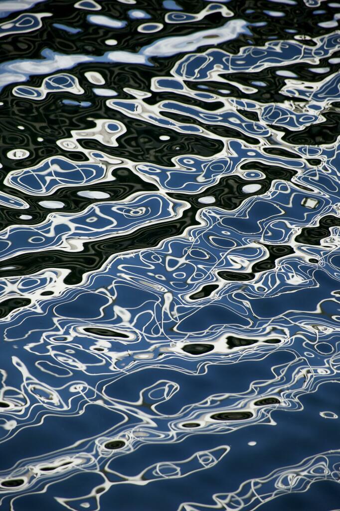 Colour image showing the reflection of a white metal walkway over a channel in a marina where the breeze and blue sky have created amazing abstract reflections in the water. Every second the patterns were subtly different.