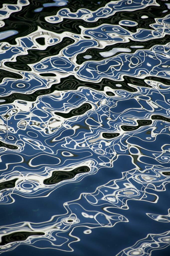 Colour image showing the reflection of a white metal walkway over a channel in a marina where the breeze and blue sky have created amazing abstract reflections in the water. Every second the patterns were subtly different.