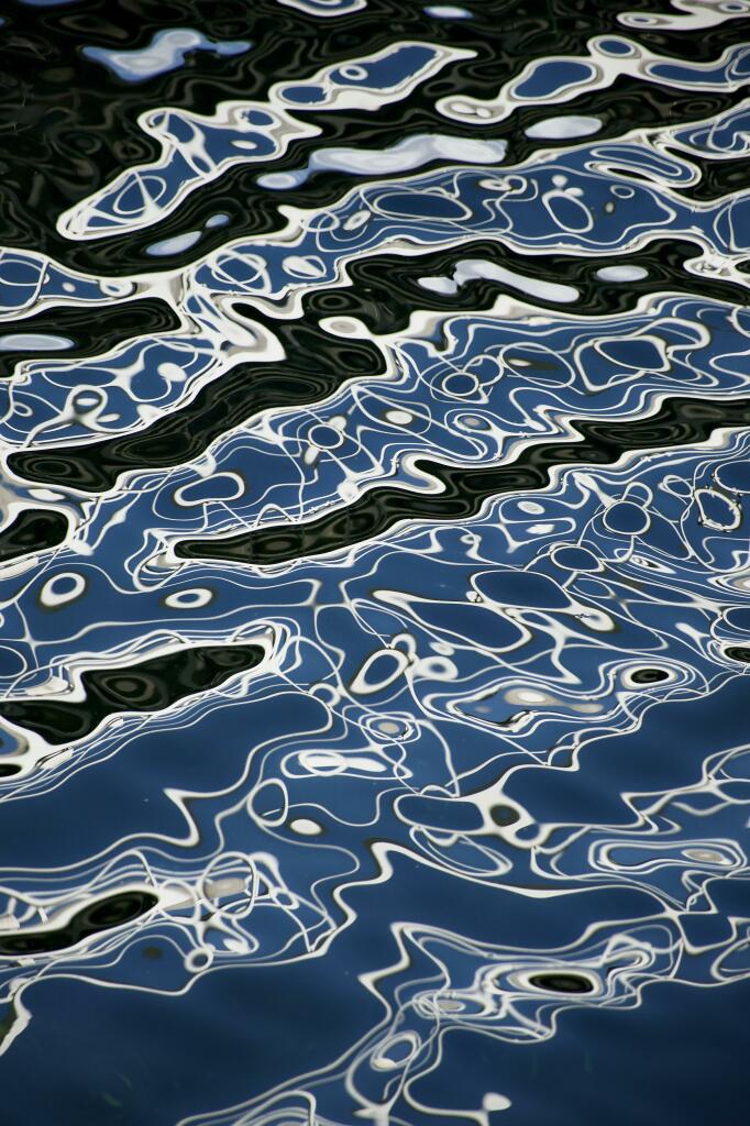 Colour image showing the reflection of a white metal walkway over a channel in a marina where the breeze and blue sky have created amazing abstract reflections in the water. Every second the patterns were subtly different.