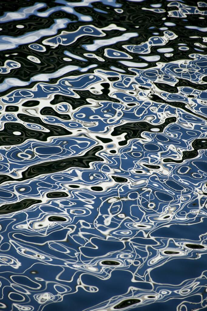 Colour image showing the reflection of a white metal walkway over a channel in a marina where the breeze and blue sky have created amazing abstract reflections in the water. Every second the patterns were subtly different.