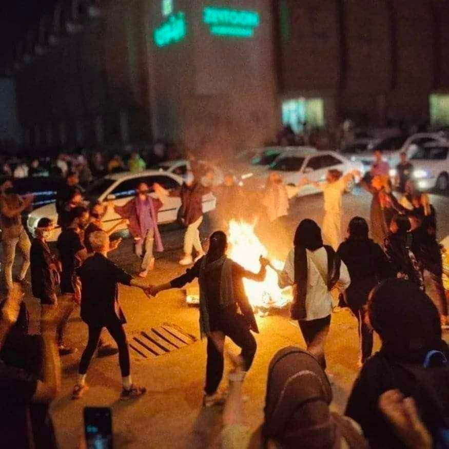 Bild einer Demonstration


Mehrere Menschen tanzen Hand in Hand um eine brennende tonne