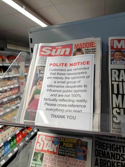 A picture of a rack of newspapers in a shop.  Someone has placed a notice in front of the Scum reading

POLITE NOTICE

CUSTOMERS ARE REMINDED THAT THESE NEWSPAPERS ARE MERELY OPINIONS OF A SMALL GROUP OF BILLIONAIRES DESPERATE TO INFLUENCE PUBLIC OPINION AND ARE NOT 100% FACTUALLY REFLECTING REALITY.  PLEASE CROSS-REFERENCE EVERYTHING YOU READ.

THANK YOU