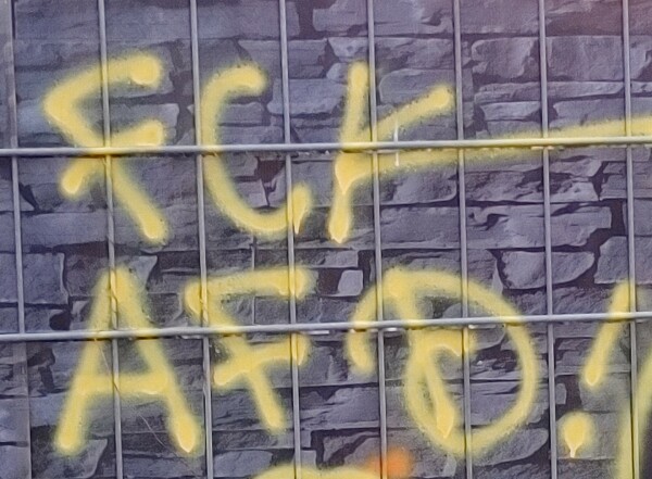 Graffito an einem Zaun Gelb auf Grau mit dem Schriftzug "FCK AFD"