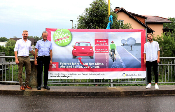 Dezernent Dr. Christopher Leo, Neidensteins Bürgermeister Frank Gobernatz und Ricardo Beringer von der Stabsstelle Nachhaltige Mobilität des Rhein-Neckar-Kreises präsentierten das großformatige Banner zum Sicherheitsabstand.