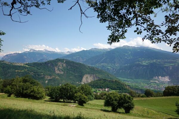 Ausblick auf weite Landschaft mit Hügeln und Bergen. Blauer Himmel mit ein paar Wolken über den Gipfeln