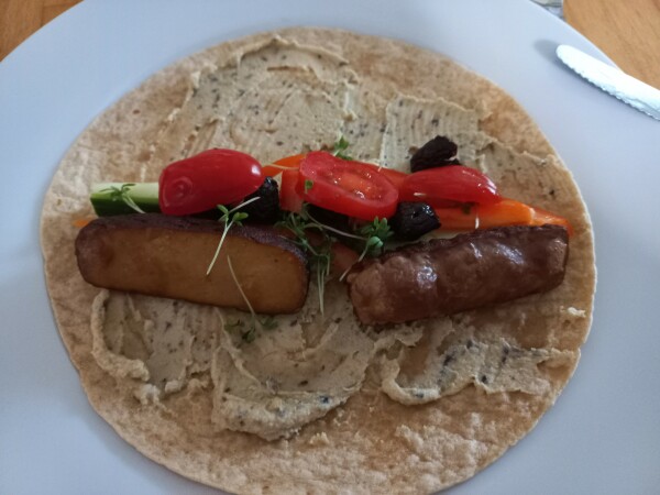 Ein Wrap, bestrichen mit Hummus, darauf diverse Gemüsesticks, 2 Scheiben Räuchertofu & Tomatenstücken