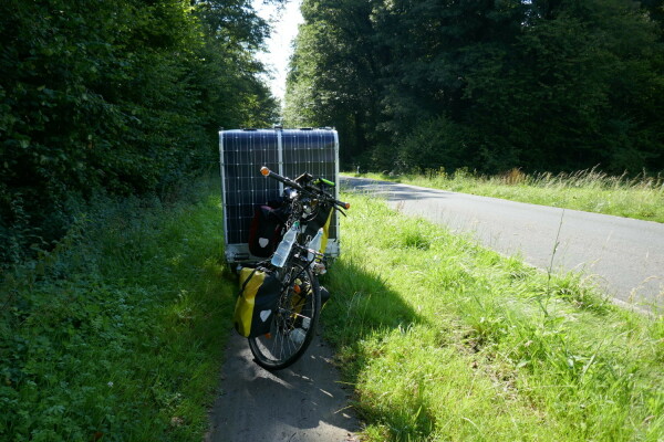 A bicycle with a small camping trailer is parked on a muddy path. The width of the path forms a lane 90 cm wide, which is completely filled by the trailer