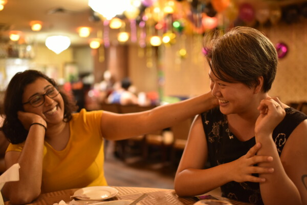 A photo of a queer couple looking happy in a restaurant