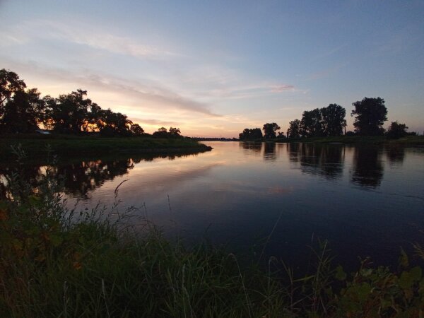 wir knien am Ufer der Elbe, dessen Wasser sich vor uns ausbreitet.
Von links leuchtet die Sonne schon aufs Wasser und man sieht am gegenüberliegenden Ufer, noch leichte Nebelschwaden über dem Wasser stehen.
Die Bäume am gegenüberliegenden Ufer spiegeln sich im leicht hellblau aussehenden Wasser