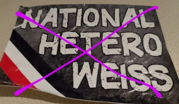 Foto/ entfernte Nazipropaganda: weiß auf schwarz "national, hetero, weiss" mit schwarz-weiß-riter Banderole unten links (alles gekreuzt mit einem lila X) 