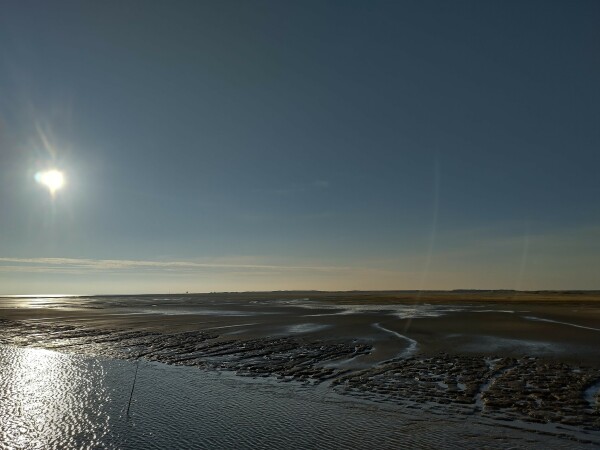 Fährfahrt zurück nach Neuharlingersiel im Gegenlicht der tiefstehenden Sonne am Nachmittag. Blick aufs Meer, in dem das Licht glitzert. Rest der Insel bei der Ausfahrt aus dem Hafen.