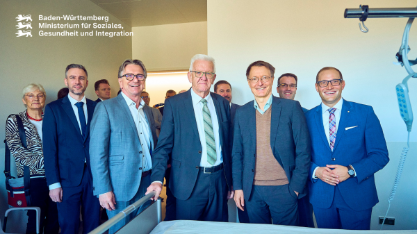 Gruppenbild hinter Klinikbett: Gesundheitsminister Manne Lucha mit Ministerpräsident Winfried Kretschmann und Bundesgesundheitsminister Karl Lauterbach.