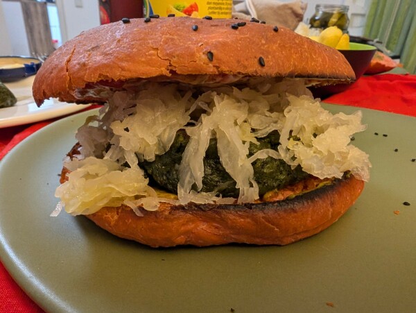 Ein Burger mit rötlichem Brötchen, grünem Patty & darauf ordentlich Sauerkraut auf einem grünen Teller 