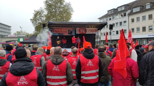 Menschen in roten Warnwesten und mit roten Fahnen vor einer Bühne