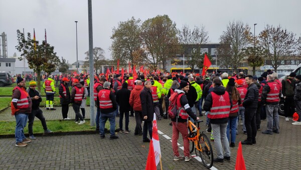 Menschen in roten Warnwesten und mit roten Fahnen versammeln sich auf einer Straße.