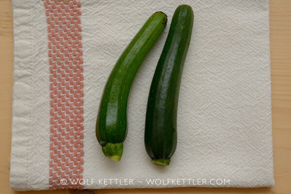 The photograph shows two small courgettes seen from above. They are displayed on a folded placemat. 